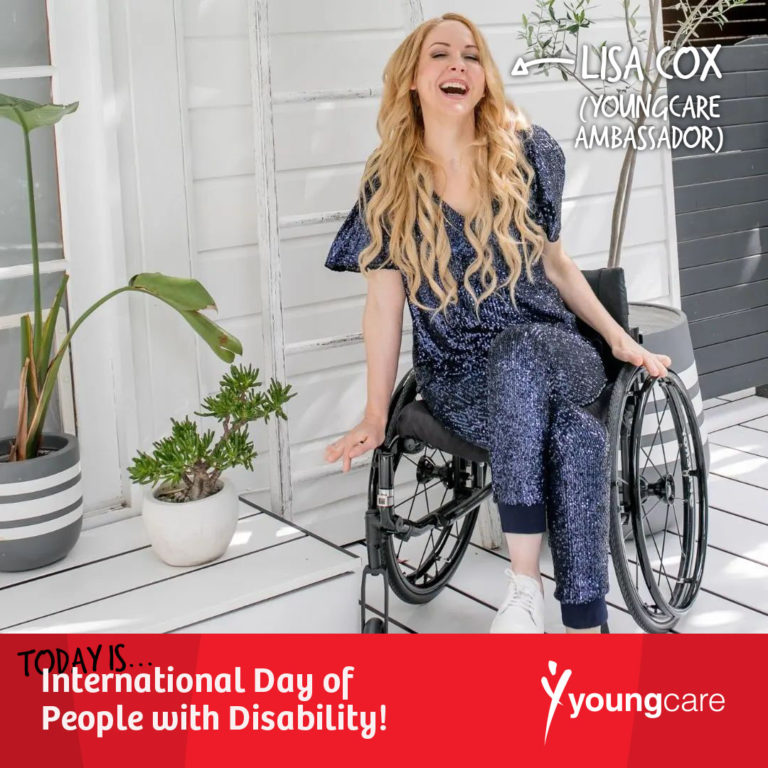 A young lady is smiling, sitting outside in a manual wheelchair. She is wearing a sparkly blue outfit and appears to be in the outdoor area of a home, surrounded by plants. 