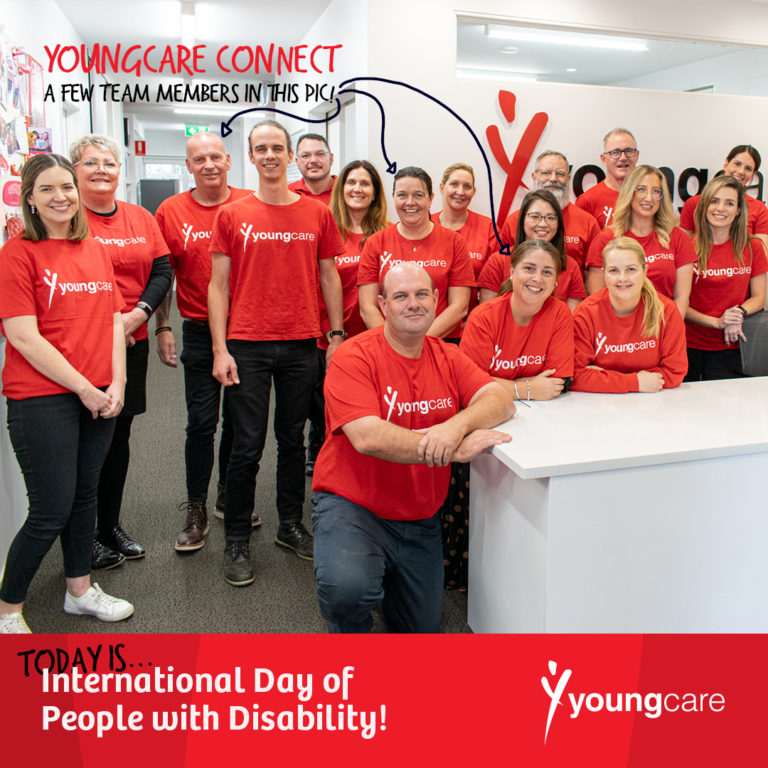 A team of people are smiling for a group photo. They're standing inside an office, and are all wearing red Youngcare shirts.