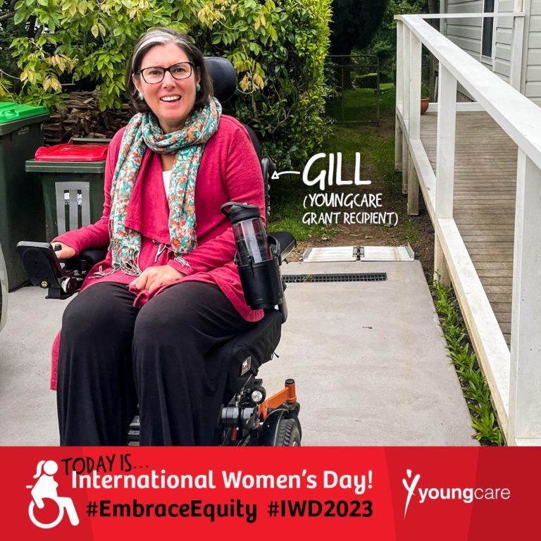 Gill is pictured outside a house on a concrete driveway. A wooden ramp to the right leads up to a weatherboard house. Surrounding the house and concrete driveway are lush trees and a grass footpath. Gill is wearing a pink top, a colourful blue scarf and black pants. Gill is sitting in an electric wheelchair. Words are positioned beside them with an arrow pointing in their direction reading "Gill (Youngcare Grant Recipient)". A banner under the image reads "Today is International Women's Day! #EmbraceEquity #IWD2023". There is a white Youngcare logo beside this text.
