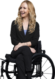 Lisa Cox, an award-winning writer, presenter, and disability advocate, is sitting in a manual wheelchair. She is wearing business clothes: a black suit jacket and pants, and a blue shirt.